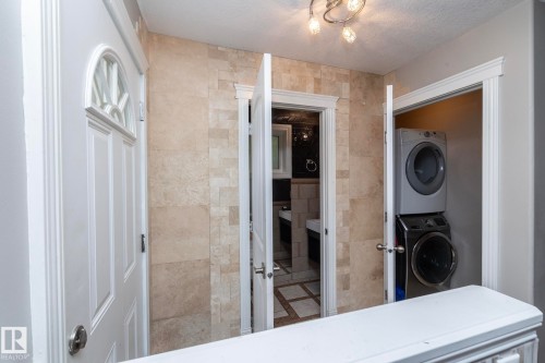 White paneled door with decorative glass inlay, tiled wall, and compact laundry area with stacked appliances - 11915 77 Street Nw, Edmonton, AB - Indoor Photo Showing Other Room