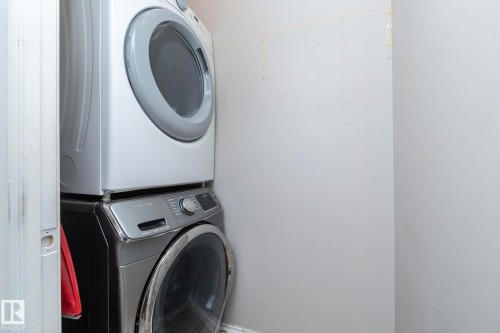 Stackable washer and dryer unit with a silver finish - 11915 77 Street Nw, Edmonton, AB - Indoor Photo Showing Laundry Room