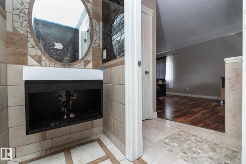 Floating vanity with integrated sink and chrome faucet, set against a tiled wall with decorative mosaic accents and an oval mirror - 11915 77 Street Nw, Edmonton, AB - Indoor Photo Showing Other Room