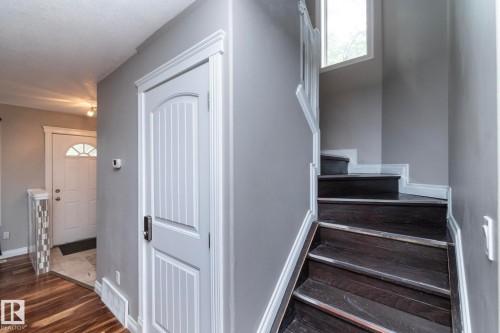 Dark wood-finish staircase with white trim, featuring a window and a white paneled door with contemporary hardware - 11915 77 Street Nw, Edmonton, AB - Indoor Photo Showing Other Room