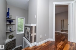 Upper-level landing featuring wood-finish flooring, a tiled half-wall, and a corner window - 