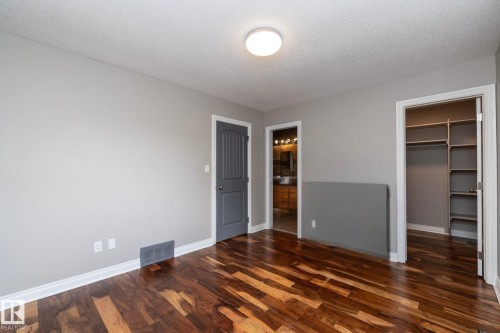 Spacious room featuring rich wood-finish flooring, light gray walls, a flush-mount ceiling light, a built-in closet with shelving, and an entryway to a bathroom with a vanity - 11915 77 Street Nw, Edmonton, AB - Indoor Photo Showing Other Room