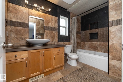 Bathroom featuring a vessel sink, wood-finish vanity, tiled walls, and a built-in bathtub - 11915 77 Street Nw, Edmonton, AB - Indoor Photo Showing Bathroom