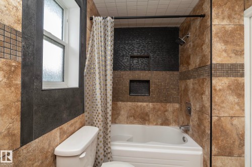 Bathroom featuring a white bathtub, decorative tiled shower surround with two recessed niches, and a white window with frosted glass - 11915 77 Street Nw, Edmonton, AB - Indoor Photo Showing Bathroom