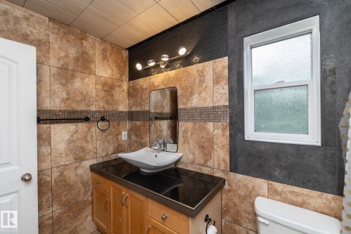 Bathroom featuring a vessel sink, wood-finish vanity with black countertop, textured wall tiling, and a window with privacy glass - 11915 77 Street Nw, Edmonton, AB - Indoor Photo Showing Bathroom