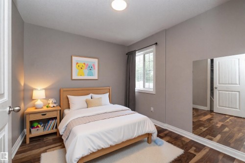 Room featuring wood-finish flooring, a double-hung window with a dark curtain, light grey painted walls, and white baseboards - 11915 77 Street Nw, Edmonton, AB - Indoor Photo Showing Bedroom