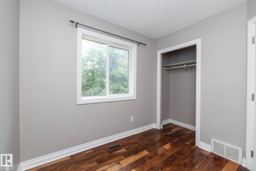 Room featuring wood-finish flooring, a window with exterior views, light gray wall paint, white baseboards, and a closet with hanging rods - 11915 77 Street Nw, Edmonton, AB - Indoor Photo Showing Other Room