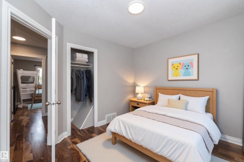 Neutral tone walls complement the wood-finish flooring in this room featuring a built-in closet with shelving - 11915 77 Street Nw, Edmonton, AB - Indoor Photo Showing Bedroom