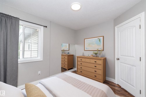 Neutral-toned room featuring a white window, wood-finish flooring, and a white paneled door - 11915 77 Street Nw, Edmonton, AB - Indoor Photo Showing Bedroom