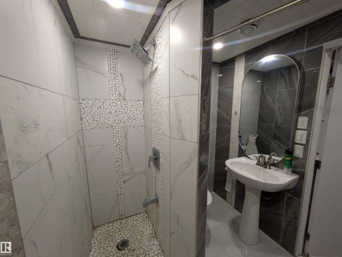 Contemporary bathroom featuring a pedestal sink with a modern faucet, an arched mirror, and a tiled shower - 11915 77 Street Nw, Edmonton, AB - Indoor Photo Showing Bathroom