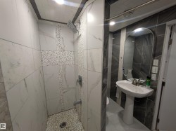 Contemporary bathroom featuring a pedestal sink with a modern faucet, an arched mirror, and a tiled shower - 