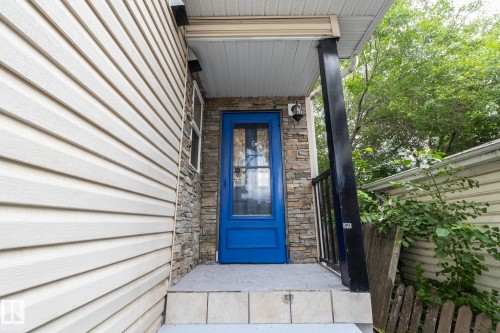 Front entrance featuring a vibrant blue door with glass insert, stacked stone facade accents, light-colored horizontal siding, covered porch, and a black railing - 11915 77 Street Nw, Edmonton, AB - Outdoor