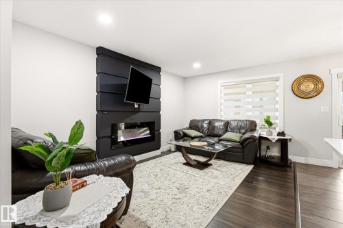 Living area featuring an electric fireplace with a dark wood-finish accent wall, dark wood-finish flooring, recessed lighting, and a window with blinds - 4317 152 Avenue Nw, Edmonton, AB - Indoor Photo Showing Living Room With Fireplace
