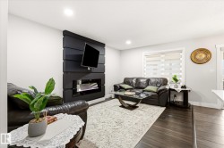 Living area featuring an electric fireplace with a dark wood-finish accent wall, dark wood-finish flooring, recessed lighting, and a window with blinds - 