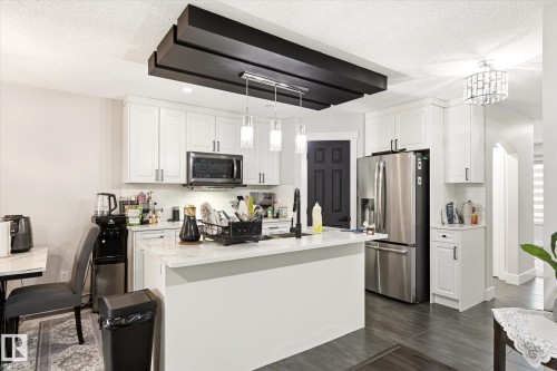 Kitchen featuring white shaker cabinetry, stainless steel appliances, a center island with a light-toned countertop, and dark wood-finish flooring - 4317 152 Avenue Nw, Edmonton, AB - Indoor Photo Showing Kitchen With Stainless Steel Kitchen With Upgraded Kitchen