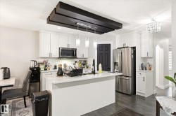 Kitchen featuring white shaker cabinetry, stainless steel appliances, a center island with a light-toned countertop, and dark wood-finish flooring - 