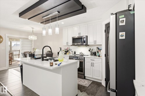 Bright kitchen featuring white shaker cabinetry, stainless steel appliances, a center island with a black faucet, and wood-finish flooring - 4317 152 Avenue Nw, Edmonton, AB - Indoor Photo Showing Kitchen With Upgraded Kitchen