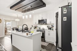 Bright kitchen featuring white shaker cabinetry, stainless steel appliances, a center island with a black faucet, and wood-finish flooring - 