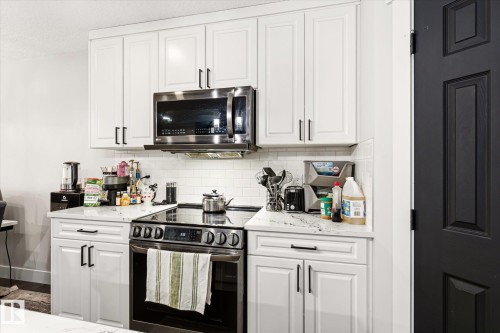 Kitchen featuring white shaker-style cabinetry with black hardware, stainless steel appliances, a subway tile backsplash, and a white countertop - 4317 152 Avenue Nw, Edmonton, AB - Indoor Photo Showing Kitchen