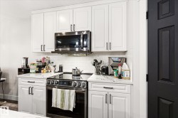 Kitchen featuring white shaker-style cabinetry with black hardware, stainless steel appliances, a subway tile backsplash, and a white countertop - 