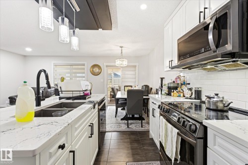 Modern kitchen featuring white cabinetry, stone-finish countertops, and stainless steel appliances - 4317 152 Avenue Nw, Edmonton, AB - Indoor Photo Showing Kitchen With Double Sink With Upgraded Kitchen