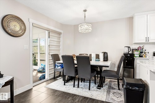 Dining area with dark wood-finish flooring, featuring a modern chandelier and direct access to the exterior through a glass sliding door with horizontal blinds - 4317 152 Avenue Nw, Edmonton, AB - Indoor Photo Showing Dining Room