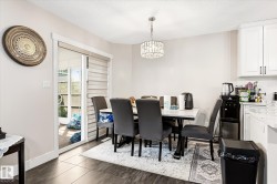 Dining area with dark wood-finish flooring, featuring a modern chandelier and direct access to the exterior through a glass sliding door with horizontal blinds - 