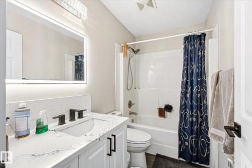 Bathroom featuring a white vanity with a solid surface countertop, an undermount sink, and matte black fixtures - 4317 152 Avenue Nw, Edmonton, AB - Indoor Photo Showing Bathroom