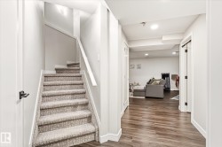 Carpeted staircase with white handrail and trim, featuring a wood-finish flooring hallway and recessed lighting - 