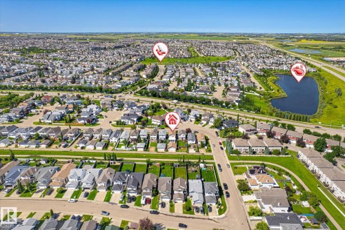 Expansive aerial perspective showcasing a residential development with numerous single-family homes and townhomes, a significant water feature, abundant green spaces, and surrounding infrastructure - 4317 152 Avenue Nw, Edmonton, AB - Outdoor With View