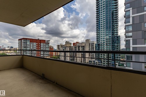 Spacious balcony featuring a concrete floor, dark metal railing, and a city skyline backdrop - #1210 10140 120 St Nw, Edmonton, AB - Outdoor With Balcony