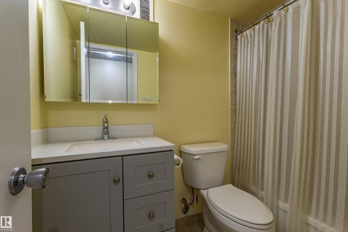 Bathroom featuring a light gray vanity with a white countertop and integrated sink, chrome faucet, and mirrored medicine cabinet - #1210 10140 120 St Nw, Edmonton, AB - Indoor Photo Showing Bathroom