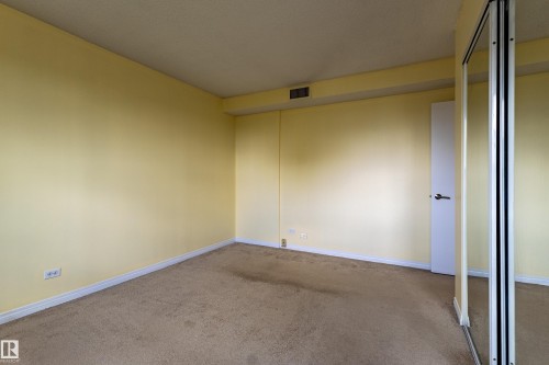 Carpeted room featuring a white interior door, mirrored sliding closet doors, and white baseboard trim - #1210 10140 120 St Nw, Edmonton, AB - Indoor Photo Showing Other Room