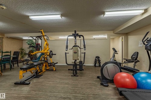 Dedicated fitness room featuring wood-finish flooring, fluorescent lighting, and neutral wall tones - #1210 10140 120 St Nw, Edmonton, AB - Indoor Photo Showing Gym Room
