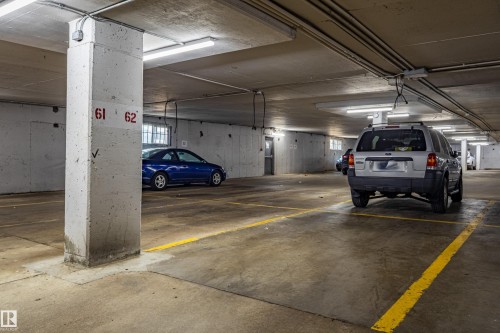Underground parking garage featuring concrete pillars, fluorescent lighting, painted yellow parking lines, and grated windows for ambient light - #1210 10140 120 St Nw, Edmonton, AB - Indoor Photo Showing Garage