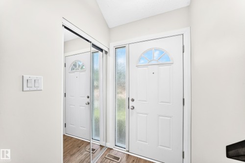 Entryway featuring a paneled front door with an arched transom window, frosted glass sidelight, wood-finish flooring, and a mirrored closet door - 3119 144 Avenue Nw, Edmonton, AB - Indoor Photo Showing Other Room