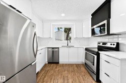 Modern kitchen featuring stainless steel appliances, white cabinetry, quartz countertops, white subway tile backsplash, and wood-finish flooring - 