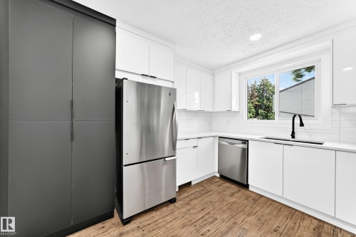 Modern kitchen featuring white cabinetry, stainless steel appliances, wood-finish flooring, white subway tile backsplash, and a black gooseneck faucet - 3119 144 Avenue Nw, Edmonton, AB - Indoor Photo Showing Kitchen