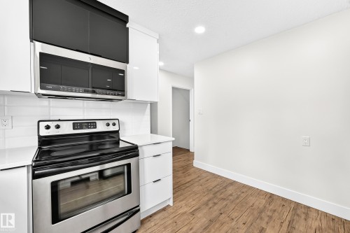 Kitchen featuring stainless steel appliances, white flat-panel cabinetry, white subway tile backsplash, light-toned countertops, and wood-finish flooring - 3119 144 Avenue Nw, Edmonton, AB - Indoor Photo Showing Kitchen