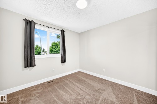 Bright room featuring a large window, neutral wall paint, white trim, and textured carpet flooring - 3119 144 Avenue Nw, Edmonton, AB - Indoor Photo Showing Other Room