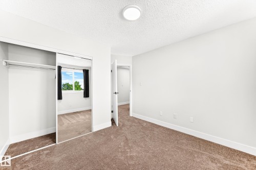 Carpeted room featuring a mirrored sliding closet door, white walls, and a round flush-mount ceiling light - 3119 144 Avenue Nw, Edmonton, AB - Indoor Photo Showing Other Room