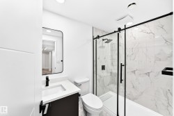 Bathroom featuring a glass-enclosed shower with black trim, a large format marbled tile surround, a built-in shower niche, and a rain shower head - 