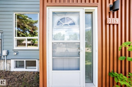 Modern exterior showcasing wood-tone vertical siding accents, a white storm door with arched grille detailing, and contemporary house numbers - 3119 144 Avenue Nw, Edmonton, AB -  With Exterior