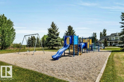 Outdoor recreation area featuring a multi-component play structure with slides and tunnels, alongside a swing set - 12 Sunset Harbour, Rural Wetaskiwin County, AB 