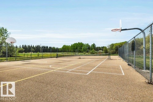 Fenced multi-sport court featuring a basketball hoop, tennis net, and clear court markings - 12 Sunset Harbour, Rural Wetaskiwin County, AB 