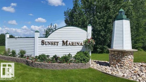 Community entrance signage featuring white horizontal siding and a decorative lighthouse structure with a river rock base - 12 Sunset Harbour, Rural Wetaskiwin County, AB 