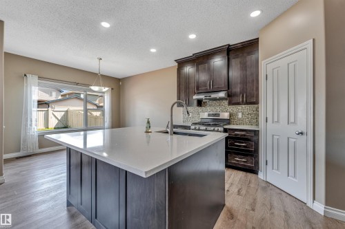 Kitchen featuring a central island with a light-toned countertop, dark wood-finish cabinetry, stainless steel appliances, a tiled backsplash, and recessed lighting - 121 64 Street Sw, Edmonton, AB - Indoor Photo Showing Kitchen With Upgraded Kitchen