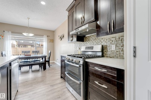 Kitchen featuring dark wood-finish cabinetry, stainless steel appliances, a patterned tile backsplash, and light-toned countertops - 121 64 Street Sw, Edmonton, AB - Indoor Photo Showing Kitchen With Upgraded Kitchen