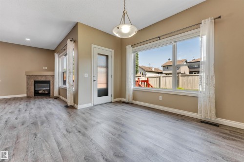 Spacious interior featuring wood-finish flooring, a contemporary fireplace with a tiled surround and mantel, a full-light exterior door, and a large picture window - 121 64 Street Sw, Edmonton, AB - Indoor With Fireplace