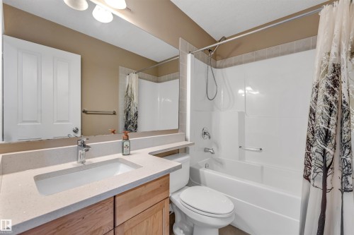 Bathroom with a single basin vanity featuring a light-toned countertop, wood-finish cabinetry, and a chrome faucet - 121 64 Street Sw, Edmonton, AB - Indoor Photo Showing Bathroom